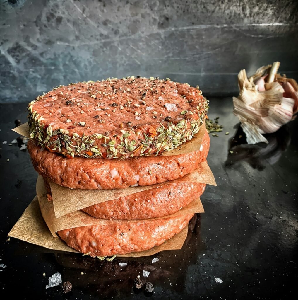 Vegan meat alternative hamburger patty stacked on top of animal meat hamburger patty.