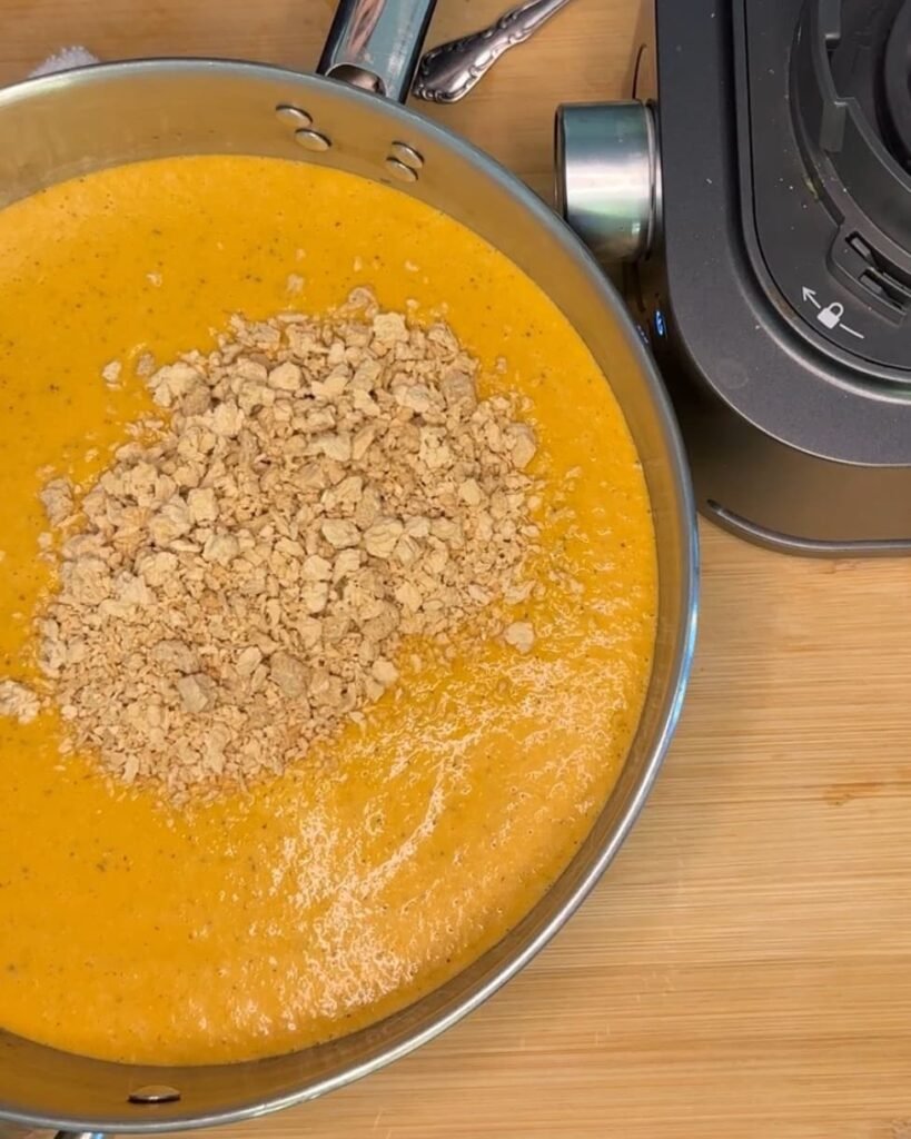 Large pot with vegan roasted red pepper sauce with a scoop of raw textured vegetable protein added and not mixed in.